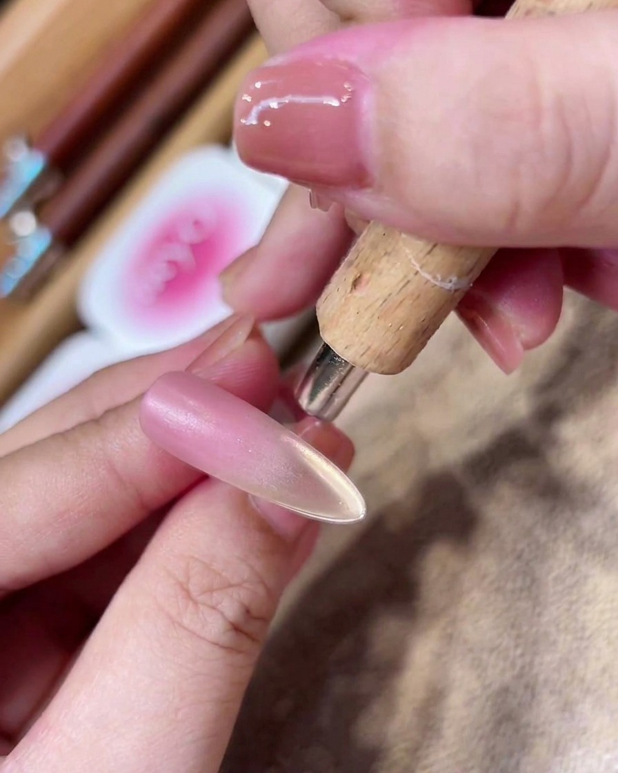 A cylindrical magnet being held near the tip of a nail to create a concentrated line of gold magnetic glitter.