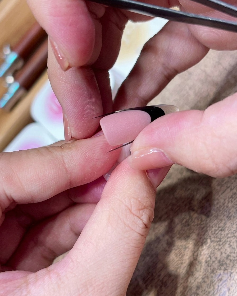 Tweezers carefully positioning a black curved sticker guide diagonally across a matte-finished nail.