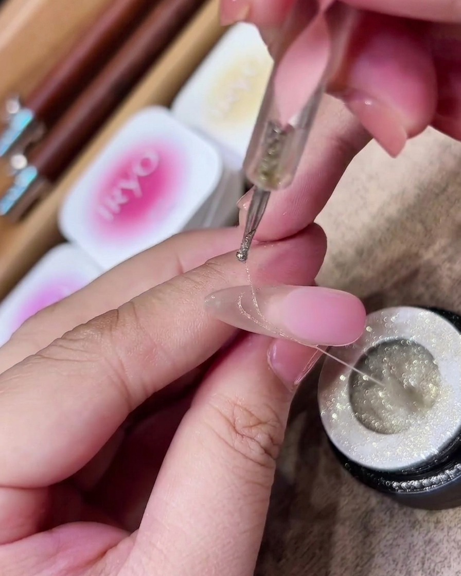Delicate, fine silver lines of spider gel being draped in artistic curves over a manicured nail.
