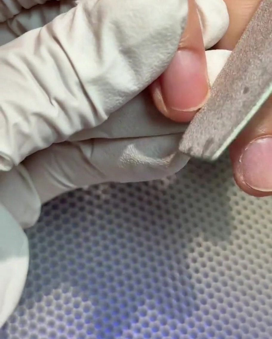 A gloved hand using a nail file to shape the free edge of a natural nail.