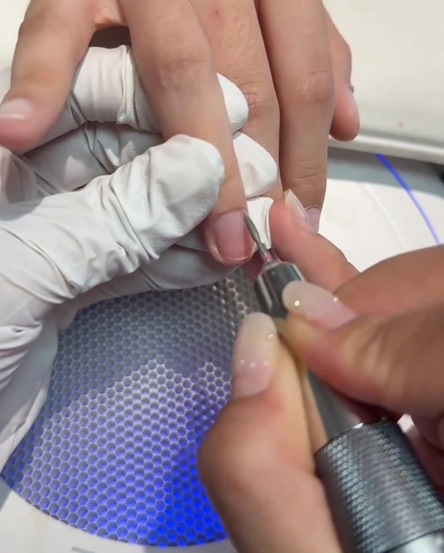 A close-up of a nail drill being used to clean and open the cuticle area of a fingernail.