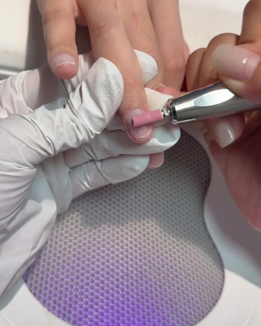 A cylindrical drill bit on a nail tool being used to buff the surface of a natural nail.