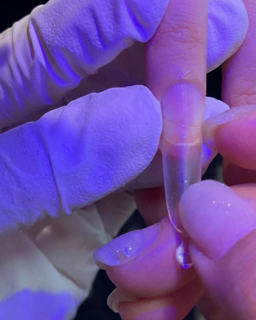 A hand pressing a clear nail extension tip onto a natural fingernail.