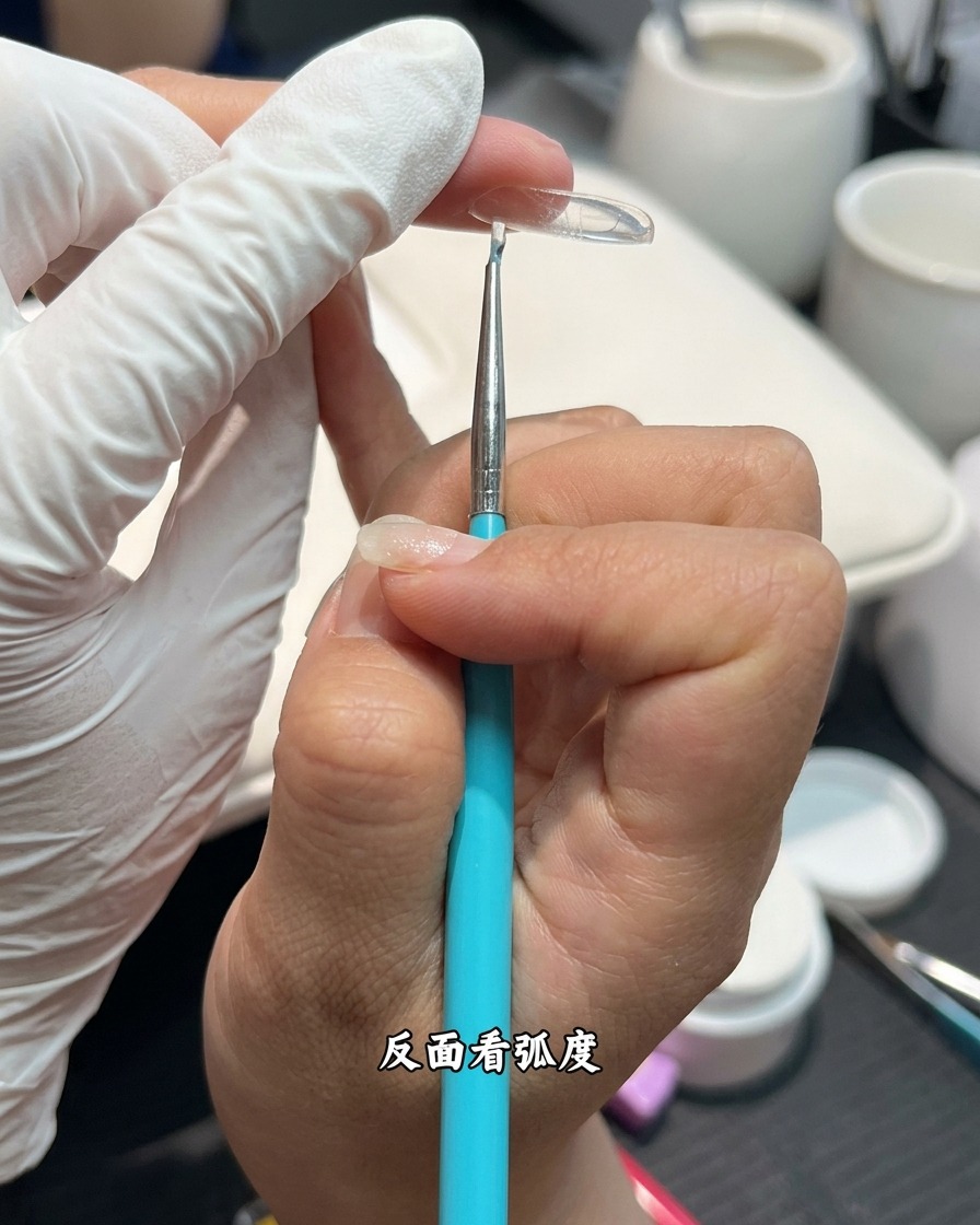 A close-up side view of a nail extension being examined for its apex and overall curvature.