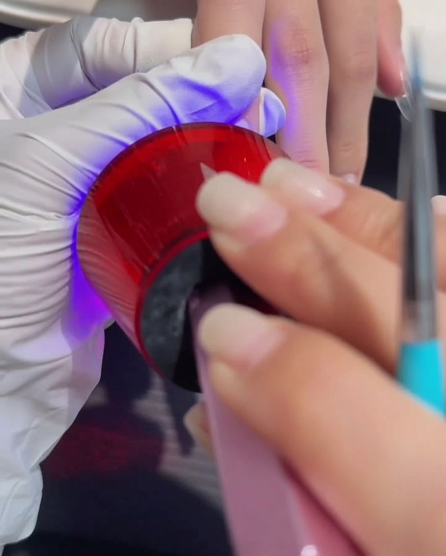 A hand placed under a professional UV/LED lamp during the gel curing process.