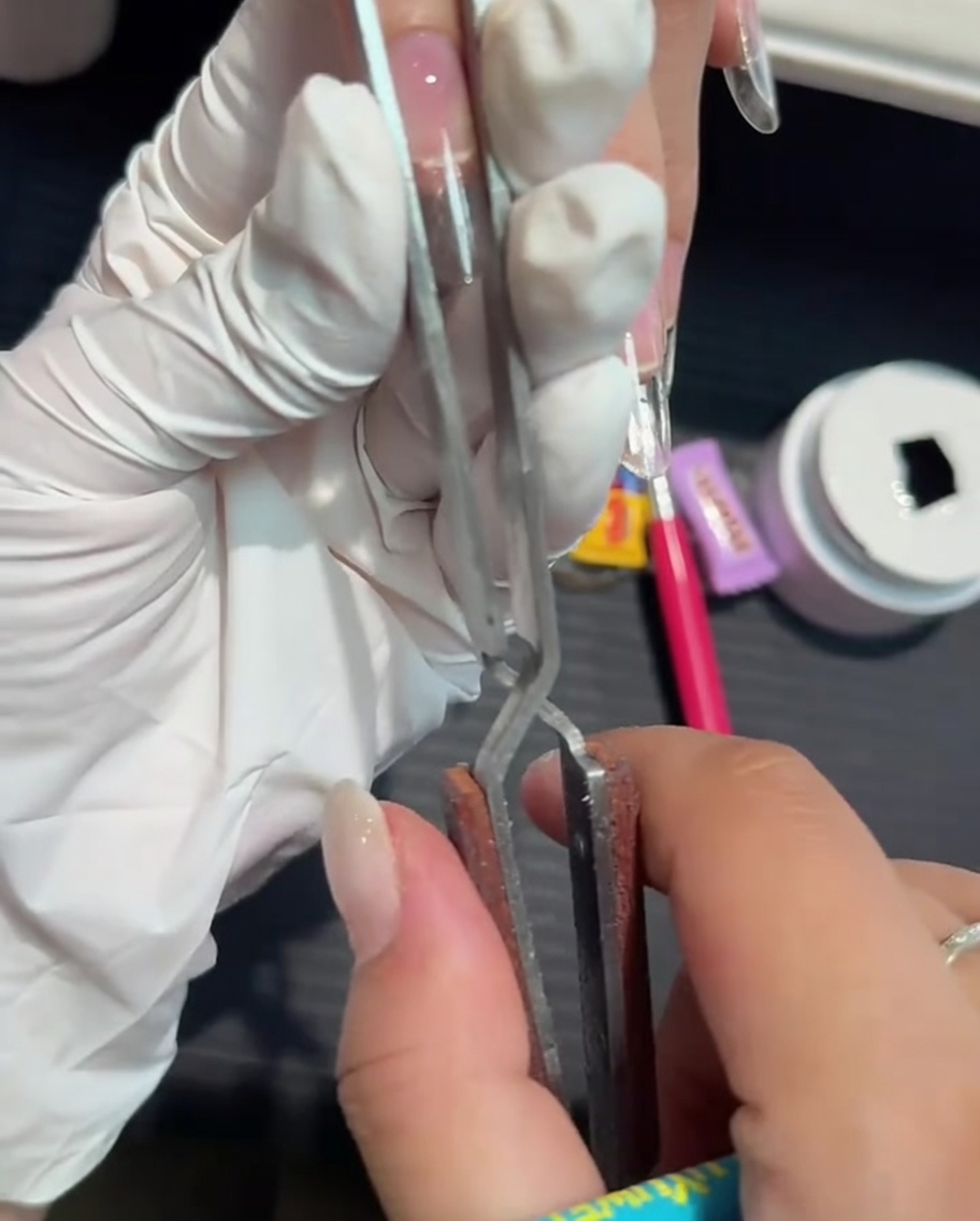 A metal nail pinching tool being used to narrow and shape a gel extension.