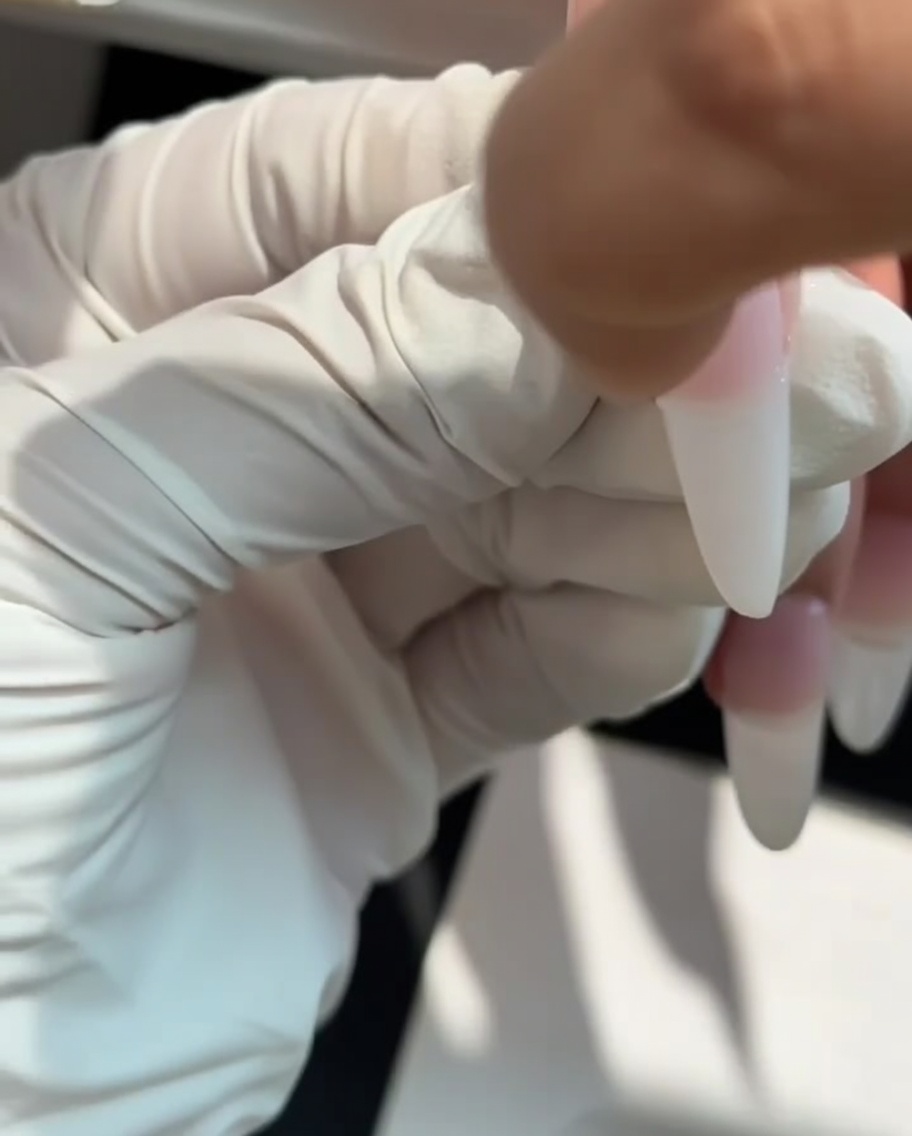 A makeup sponge being used to pat milky white gel onto the tip of a nail to create an ombre effect.
