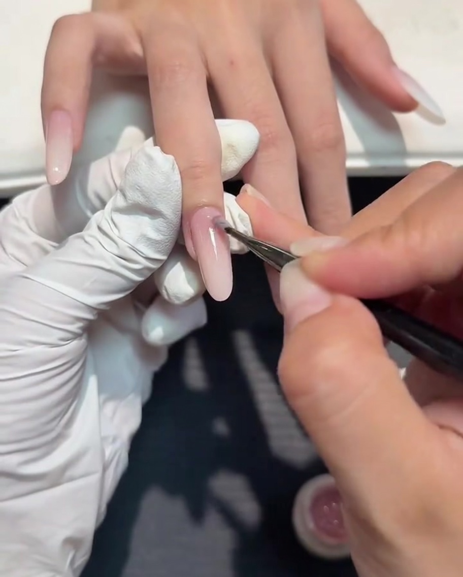 A small nail art brush applying a thin layer of nude gel over a milky white gradient.