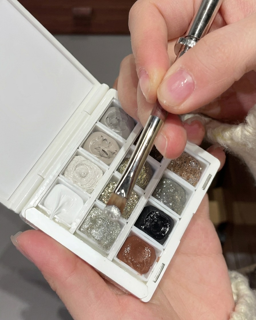 A brush mixing fine silver glitter gel with larger silver sequins on a white nail art palette.