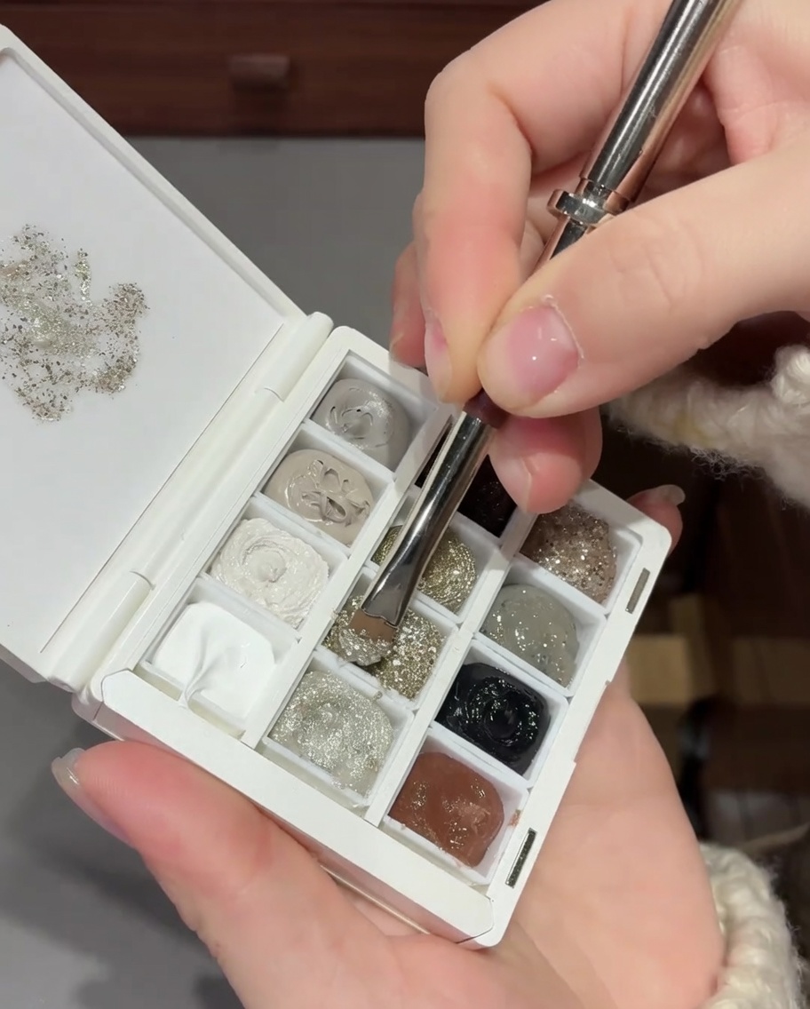 A close-up view of a brush blending silver glitter on a nail to create a smooth gradient effect.