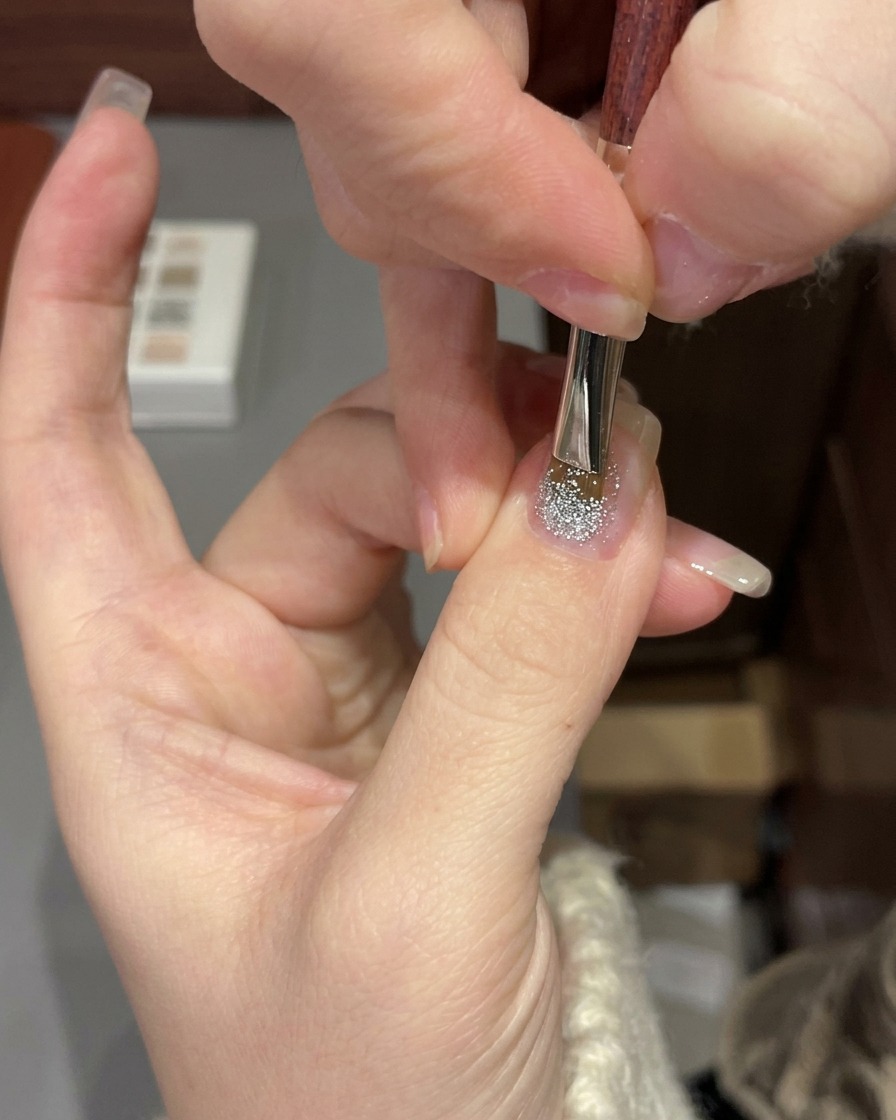 A hand positioned under a professional UV/LED nail lamp curing a glitter gel manicure.