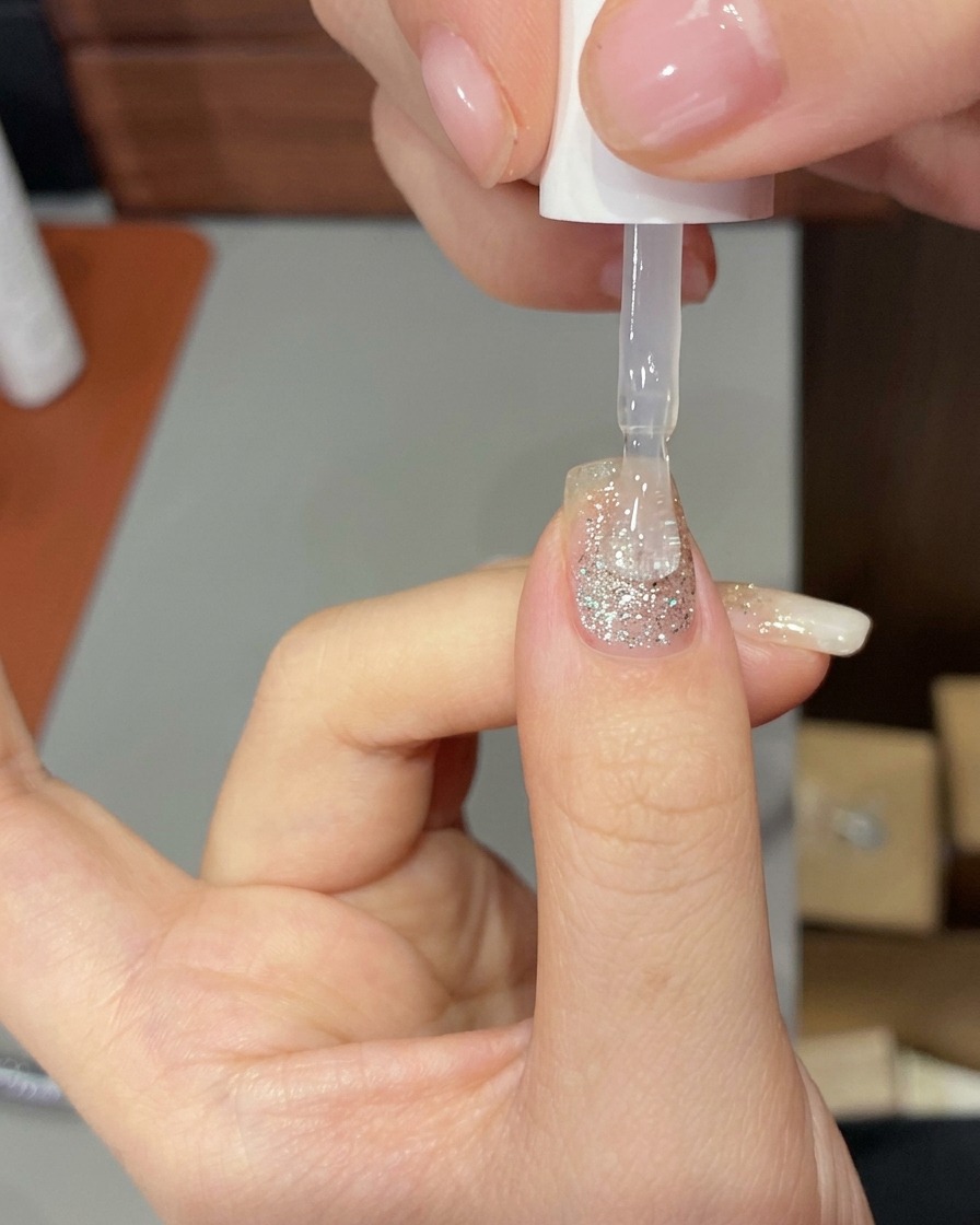 A hand positioned inside a professional UV/LED nail lamp, with the nails illuminated by the curing light.