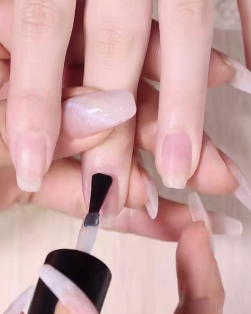 A nail brush applying a smooth layer of clear base coat to a clean natural nail.