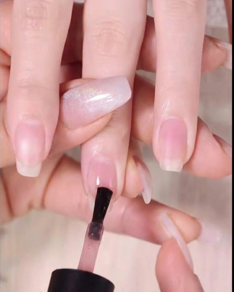 A nail polish brush applying dark amber gel to the top third of the nail tip.
