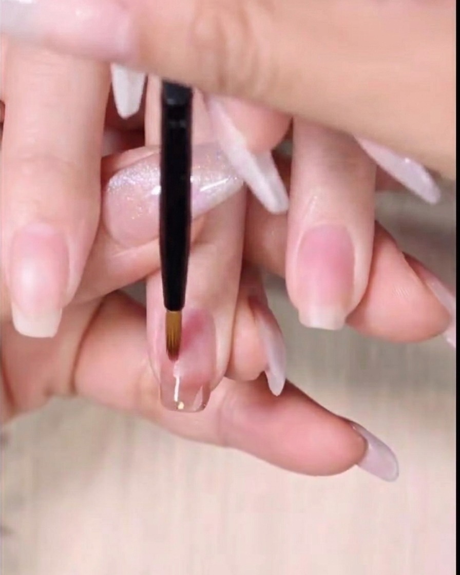 A fine detailing brush sweeping the bottom edge of wet amber gel polish downward to create a gradient.