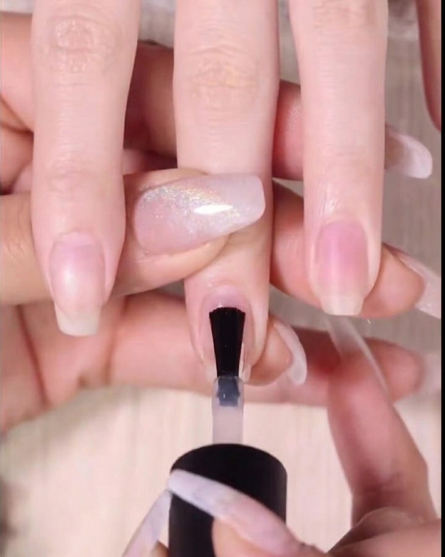 A close-up of a brush applying red gel polish to the upper two-thirds of a fingernail.