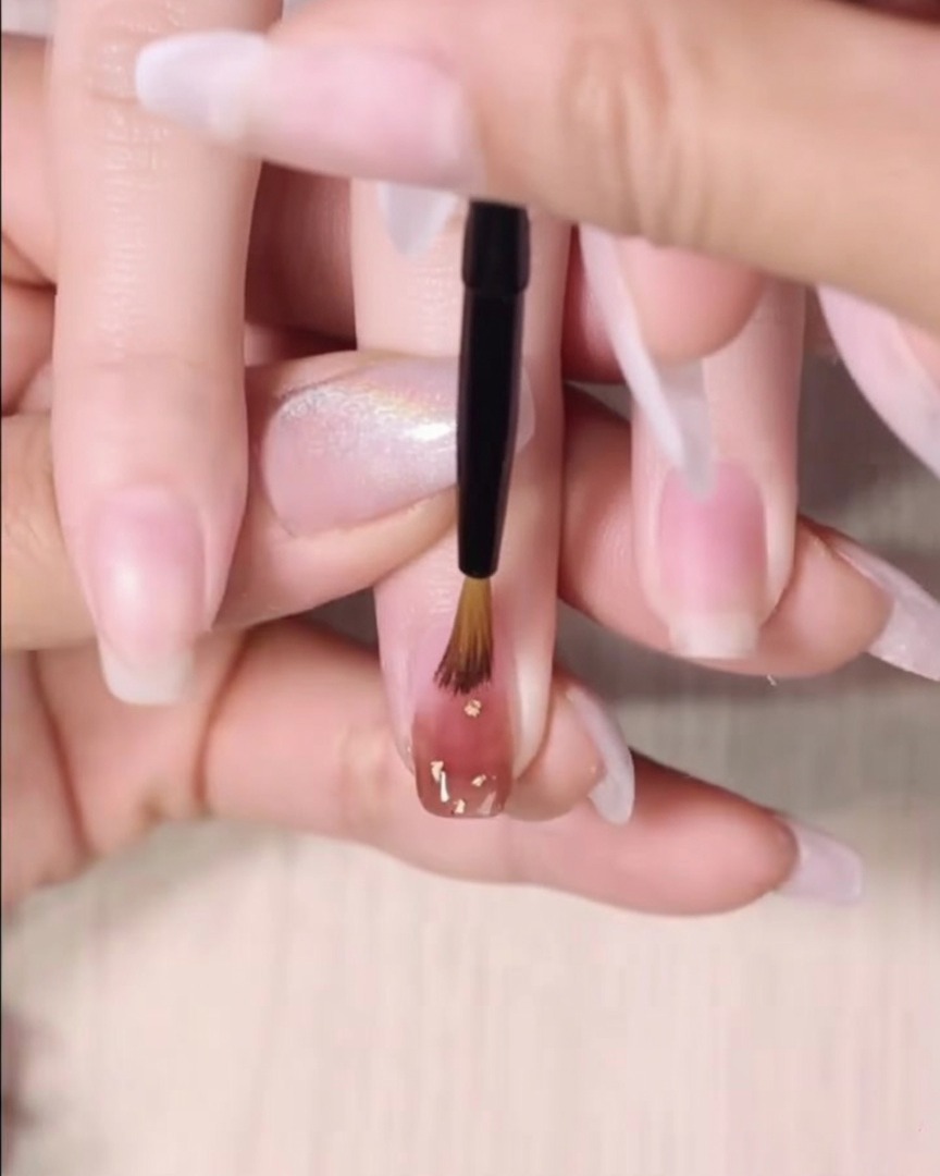 A fine detailing brush feathering the bottom edge of a second wet layer of amber gel polish.
