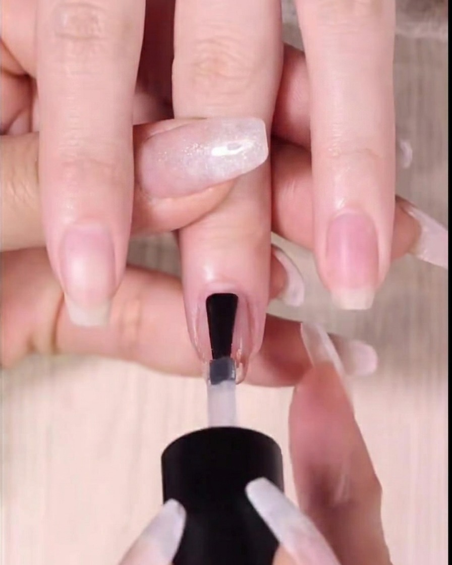 A close-up shot of a clear glossy top coat being applied over the completed red gradient nail design.
