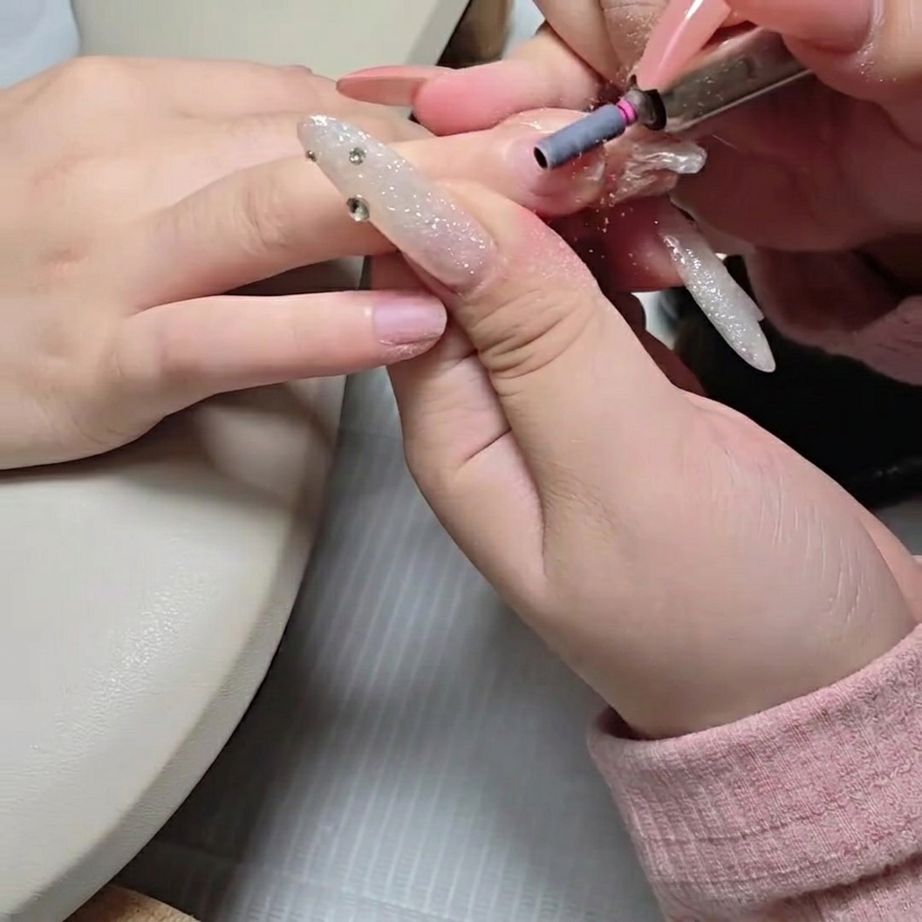 A sanding band on an e-file attachment lightly buffing the natural nail plate.