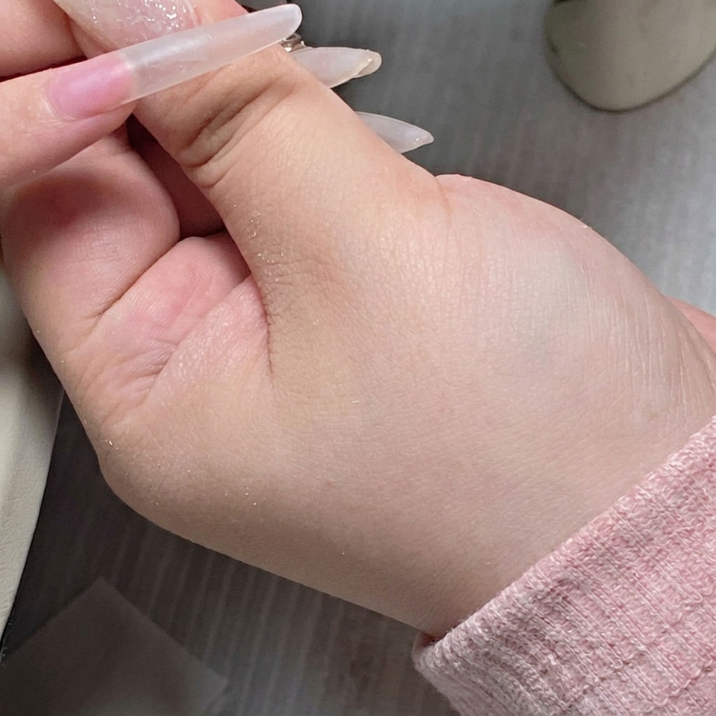 A brush from a gel bottle applying a clear base gel onto the center of a nail plate.