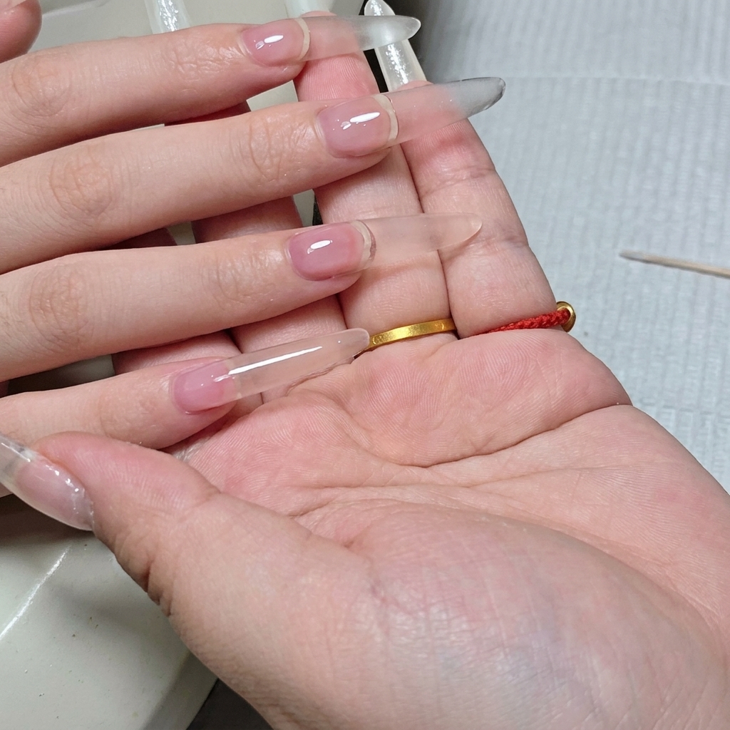 A side profile view showing the finished, structured clear nail extension, highlighting its plump and even shape.