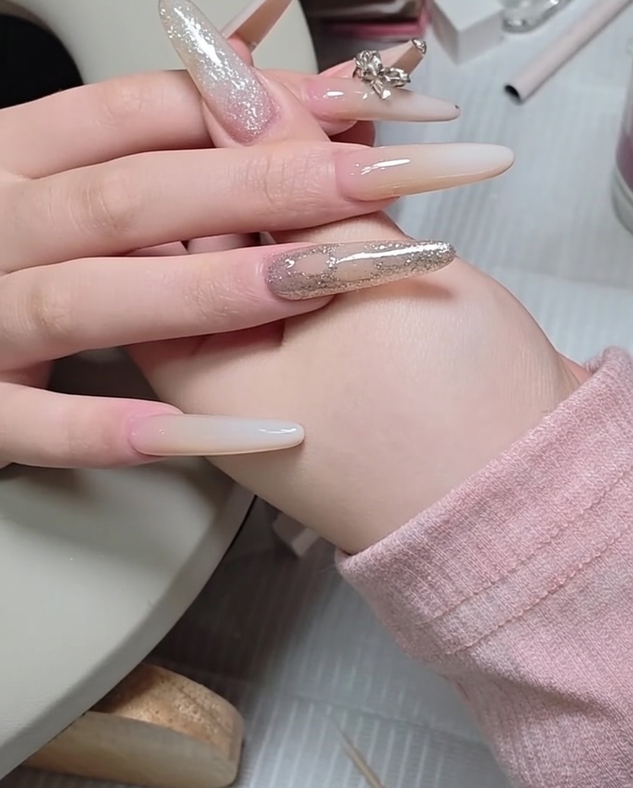 A metal cuticle pusher being used to nudge and align a small rhinestone on the surface of a manicured nail.