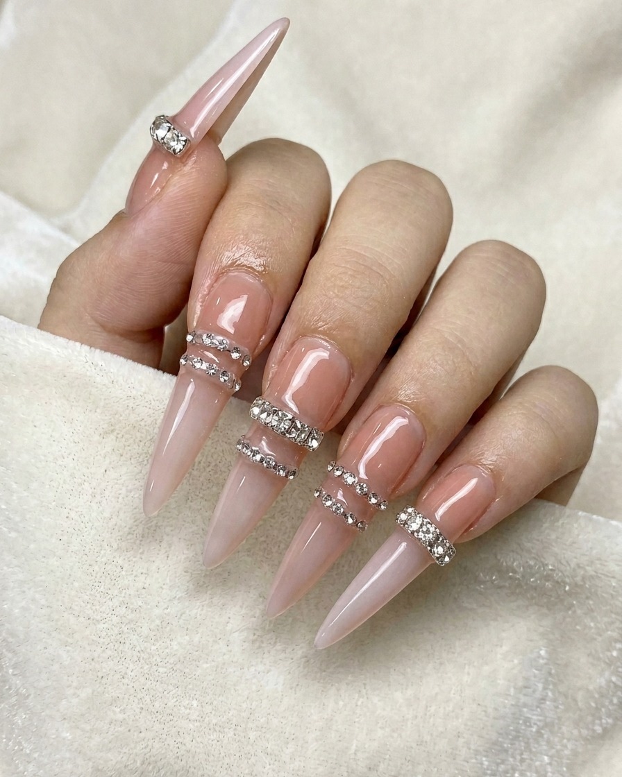 A wax pencil placing tiny clear rhinestones in a horizontal row on a nude-colored nail.