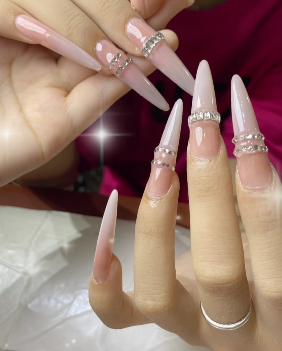 A hand under a UV lamp, showing the nails with rhinestones curing.