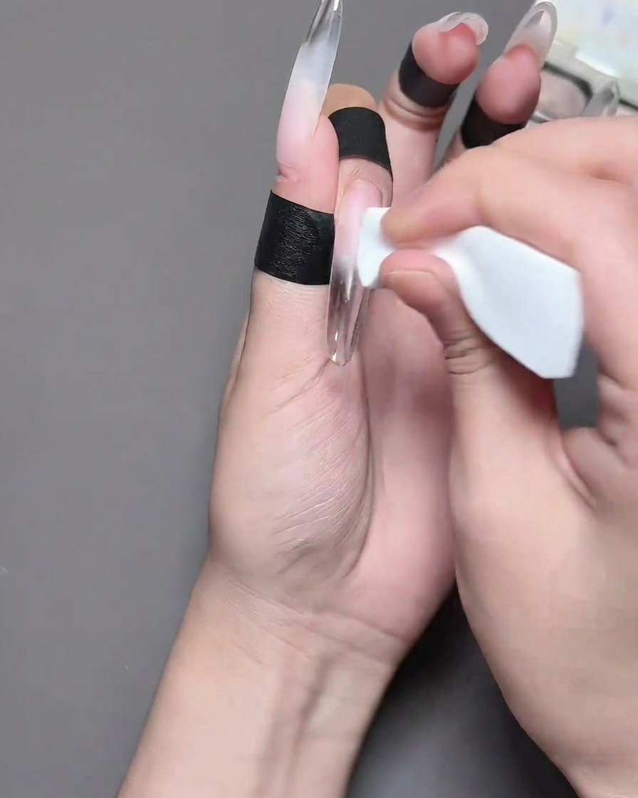 A close-up of a finger with a black barrier tape strip being applied to the skin around the nail plate.