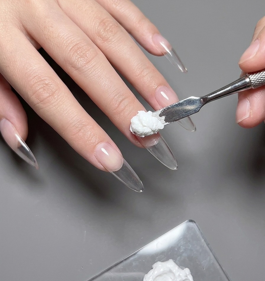 A close-up view of a liner brush carefully applying colored gel to fill in a heart stencil on a thumbnail.