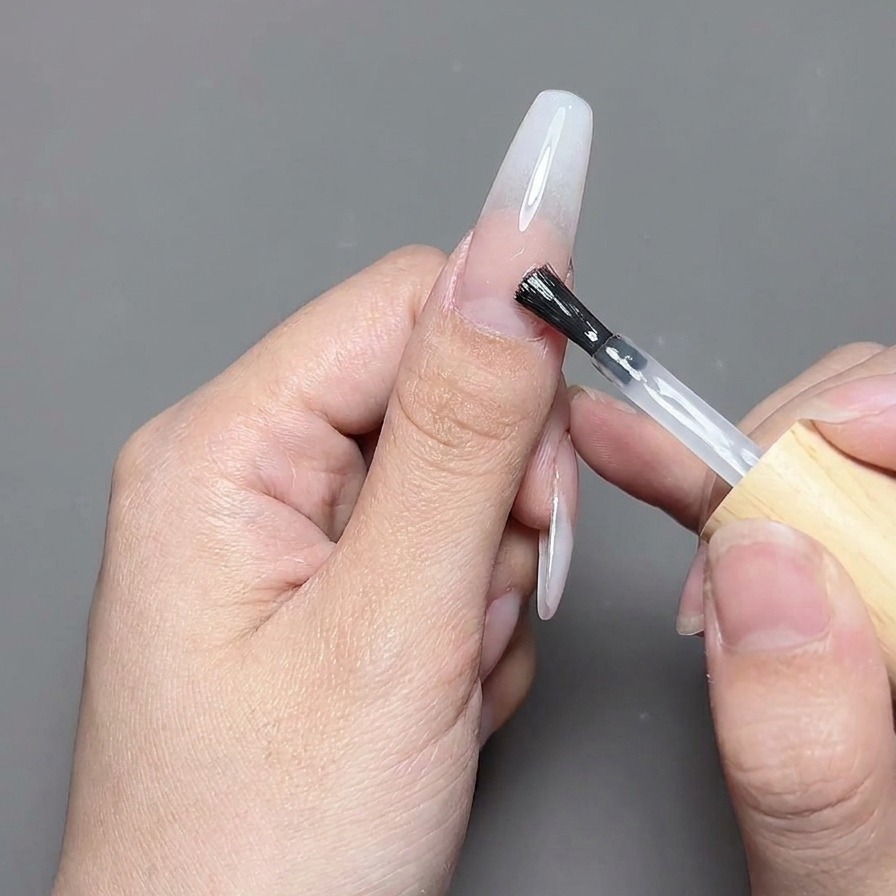 A top coat brush applying a clear, glossy gel top coat over a finished nail design.