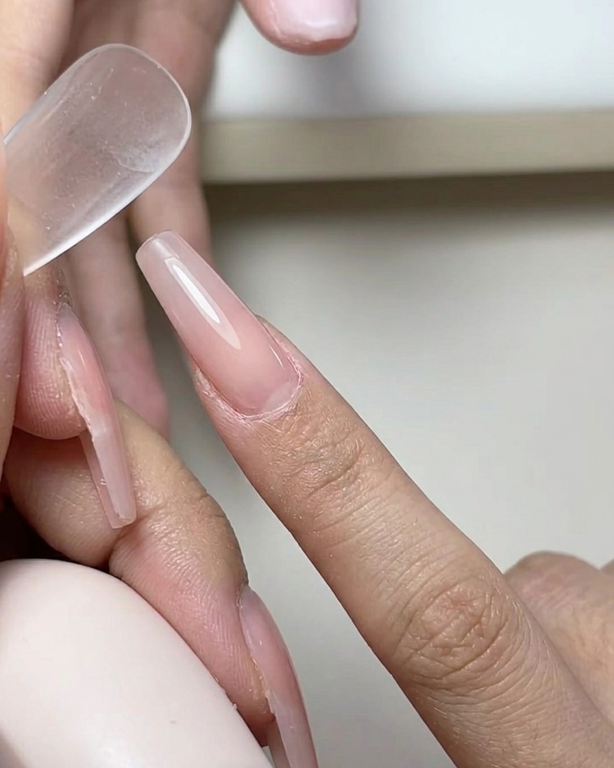 A brush applying a smooth, clear layer of gel base coat onto a natural nail surface.