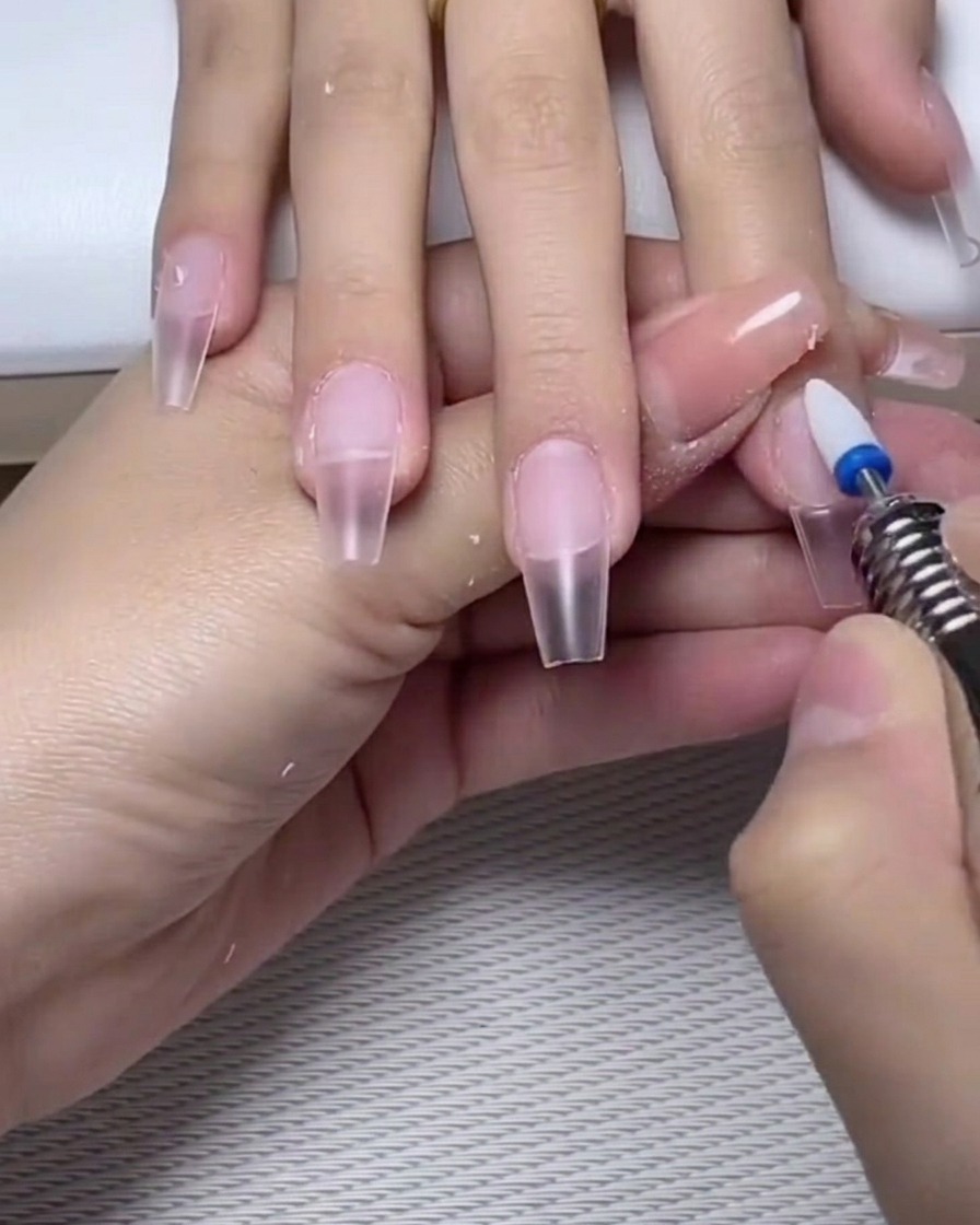 A nail file lightly buffing the surface of a cured gel base coat on the nail.