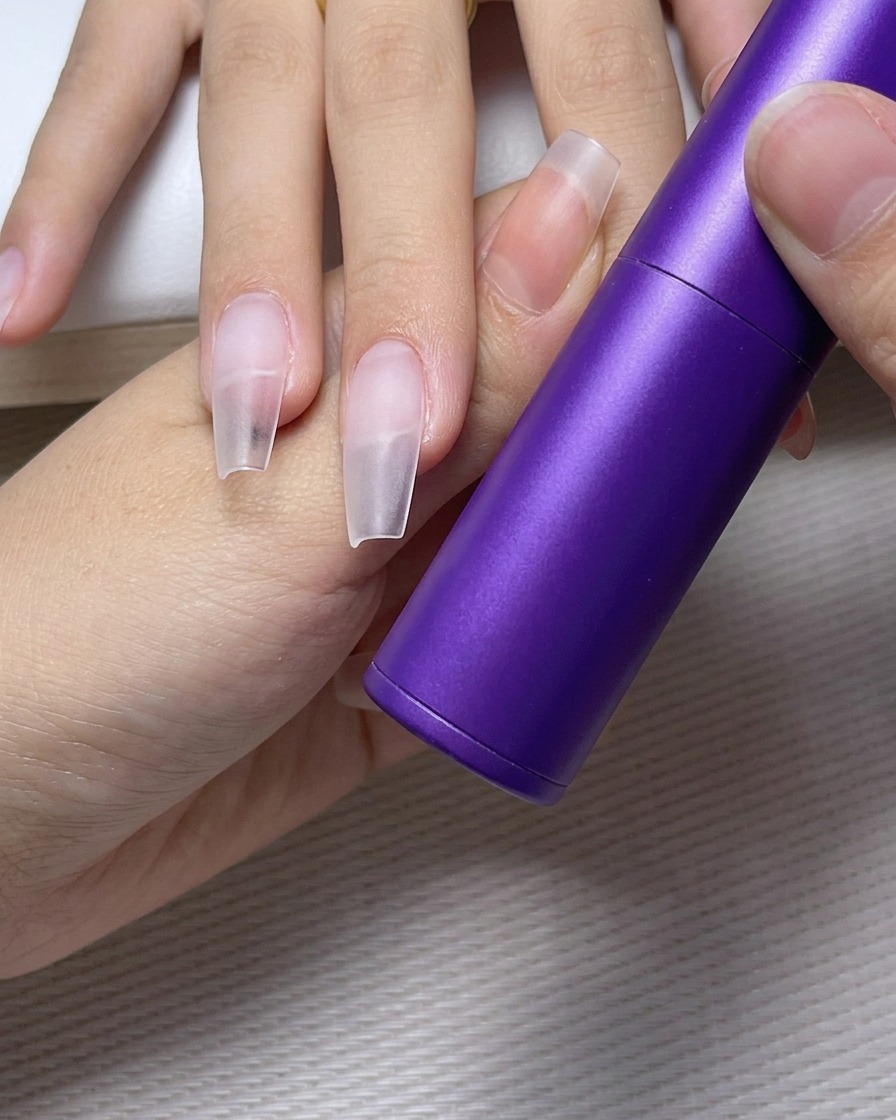 Tweezers carefully placing a small clear rhinestone onto a pre-glued spot on a polished nail.