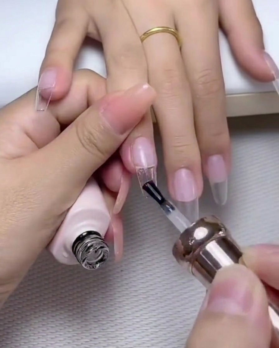 A brush applying a coat of glossy top gel over a nail decorated with pearls and rhinestones.