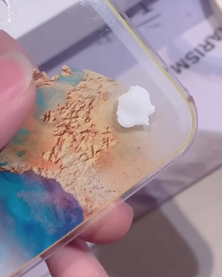 A small dollop of opaque white color gel resting on a clear acrylic mixing palette over a colorful background.