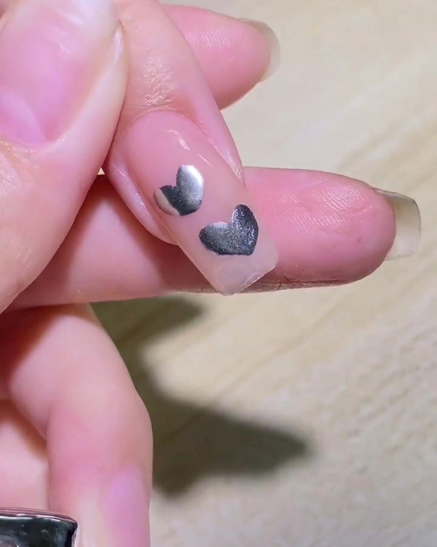 A close-up of intersecting silver lines being drawn on a nail to create a star shape.