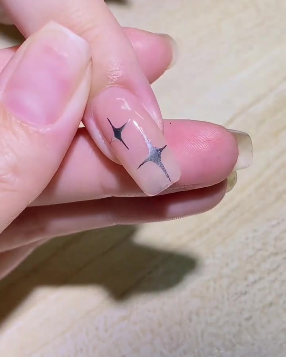 A liner brush drawing the curved outline of a butterfly wing on the side of a nail.