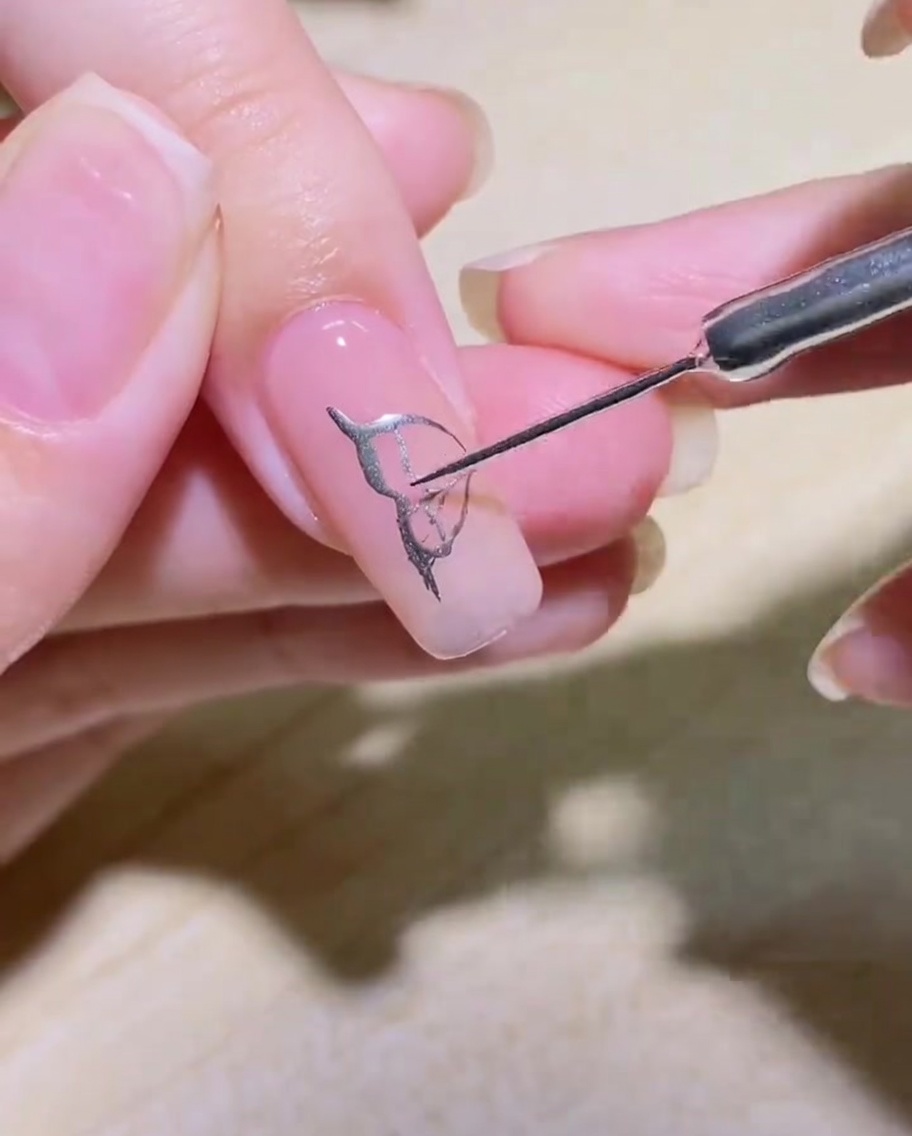 A close-up of a silver-filled butterfly wing design with delicate internal detailing on a nail.