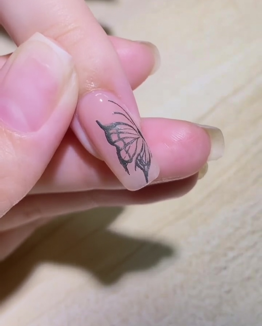 A close-up view of a nail being outlined with a silver metallic liner brush to form a flame pattern.