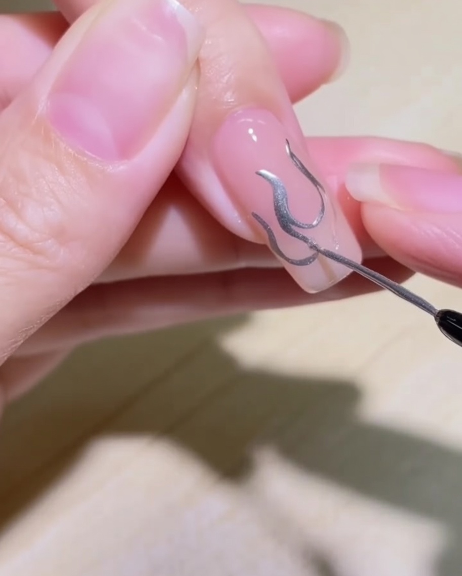 A close-up showing the flame design on the nail being filled in with silver metallic gel.