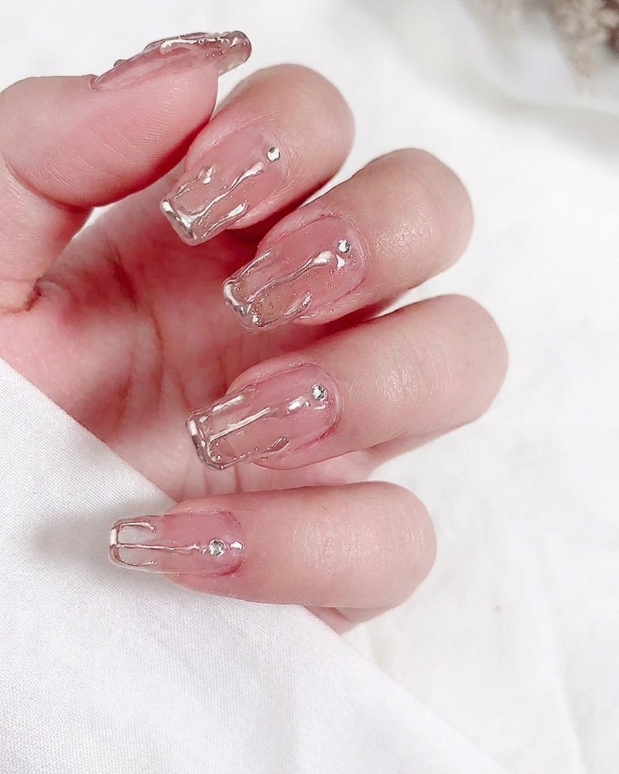 A close-up of a brush applying a coat of sheer nude gel polish to a natural fingernail.