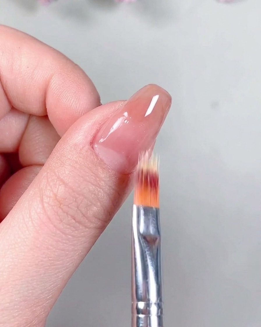 A brush applying a clear, matte-finish top coat over the cured nude gel base.
