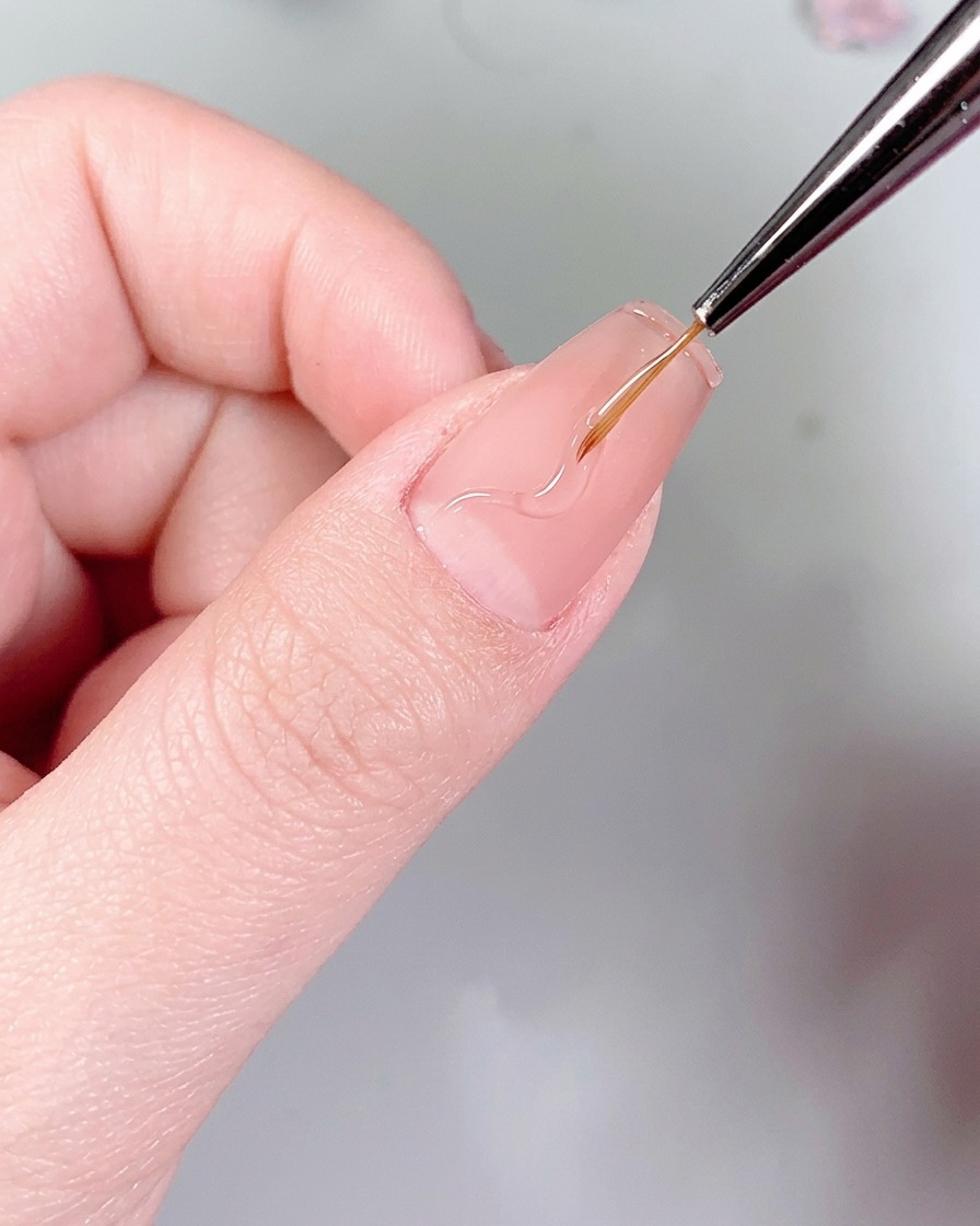 A fine liner brush drawing delicate, wavy flame patterns on a nail using clear nail glue.