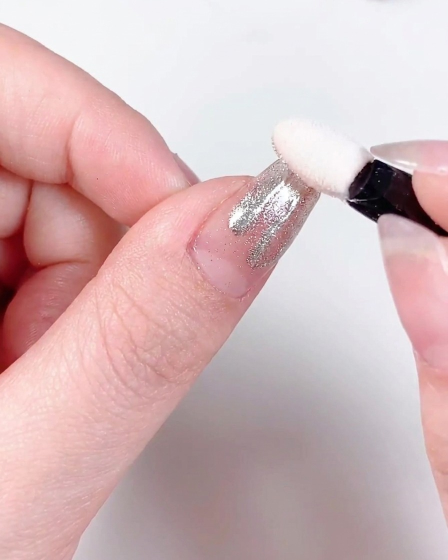 A close-up of a finger with chrome-dusted flame patterns being cured under a professional nail UV/LED lamp.
