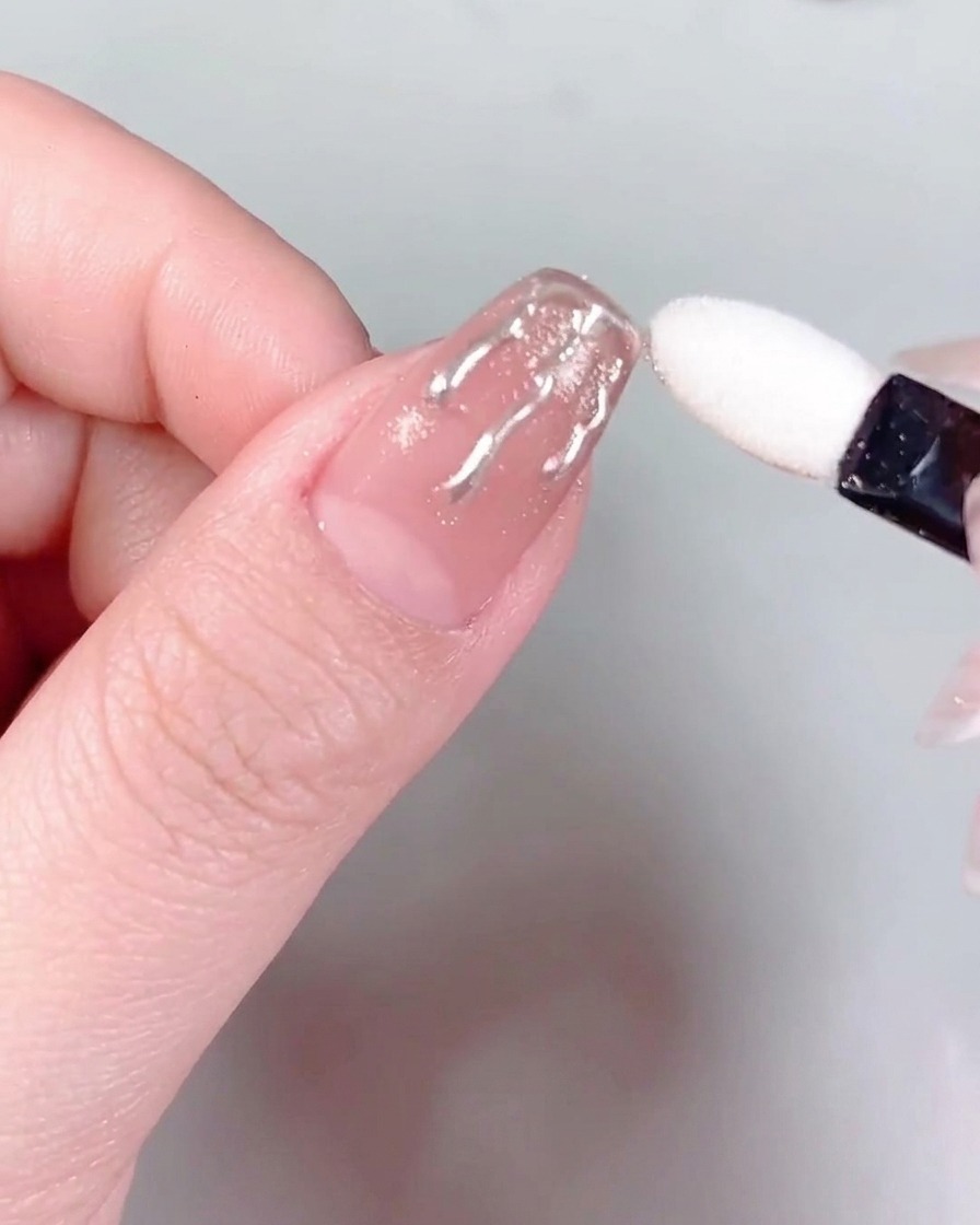 Tweezers holding a small, sparkling rhinestone and positioning it at the base of a manicured fingernail.