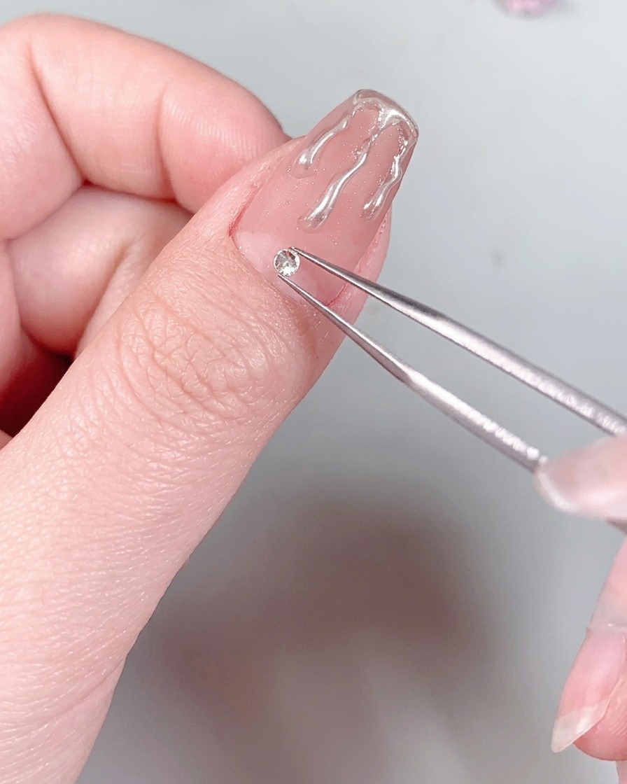 A manicured nail with a rhinestone at the base held under the light of a UV/LED nail lamp.