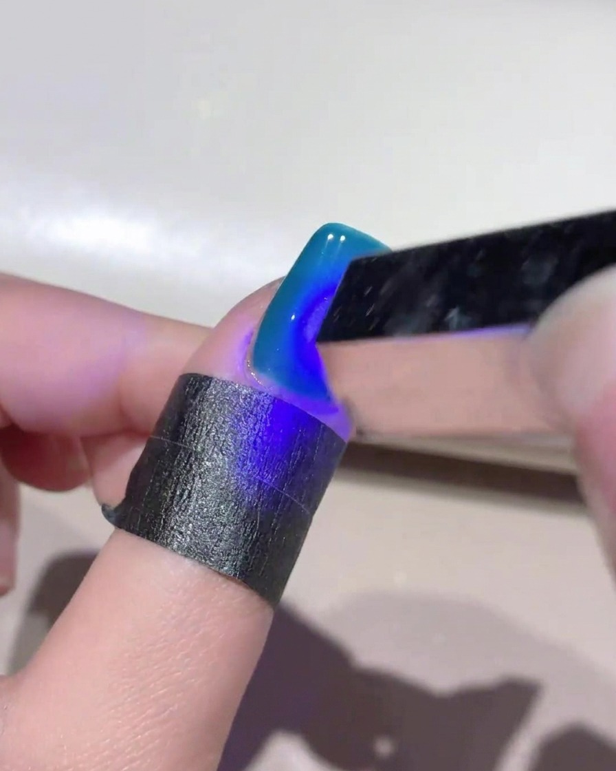 A mini handheld UV lamp shining blue light over a deep blue cat-eye gel nail to cure the design.