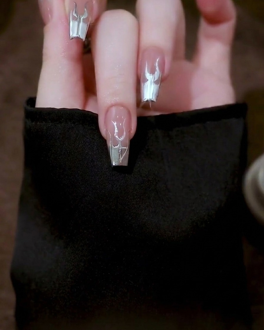 A close-up showing the finalized, detailed silver flame design on a clear nail tip.