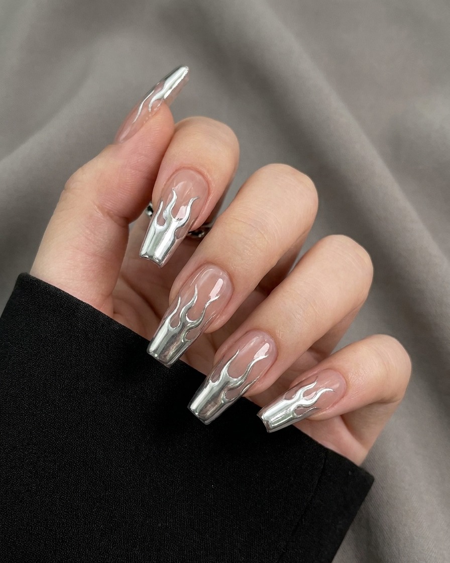 A close-up view of a brush filling in the outlined flame shapes on a nail with a highly reflective, metallic silver gel.